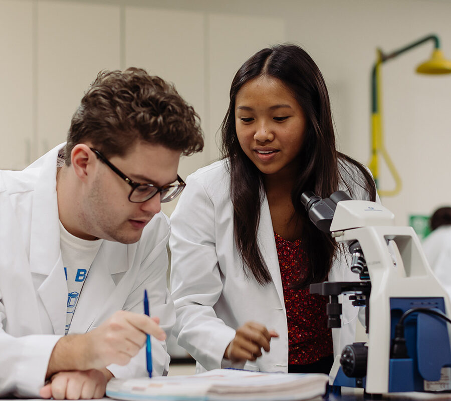 two biology students in a laboratory looking at a specimen in a microscope