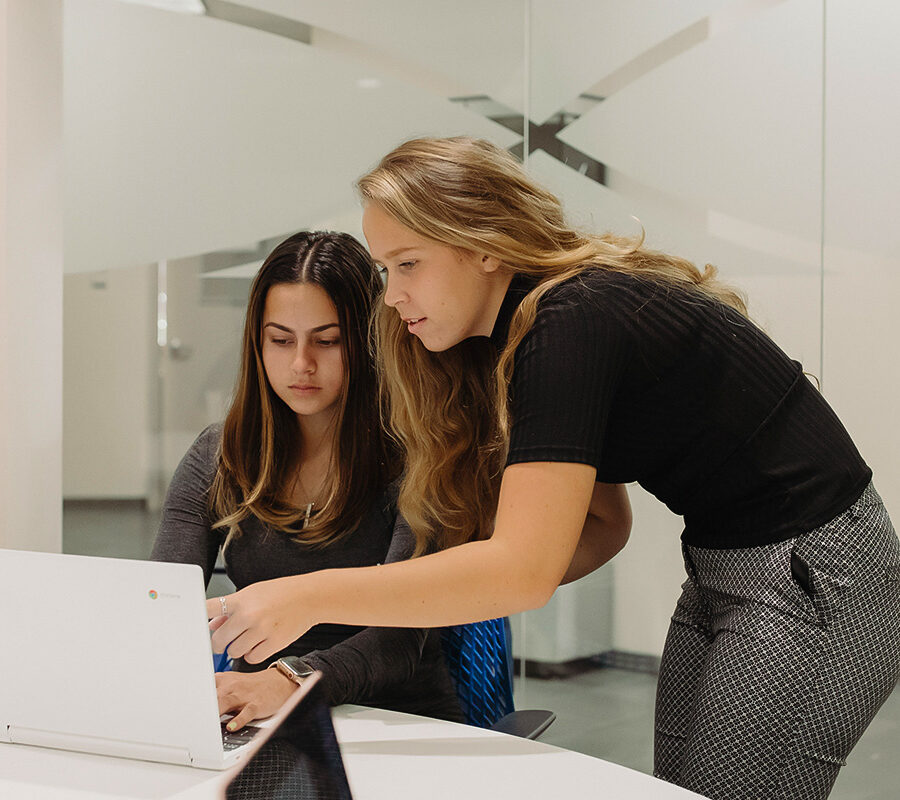 two students look at a computer screen in the library