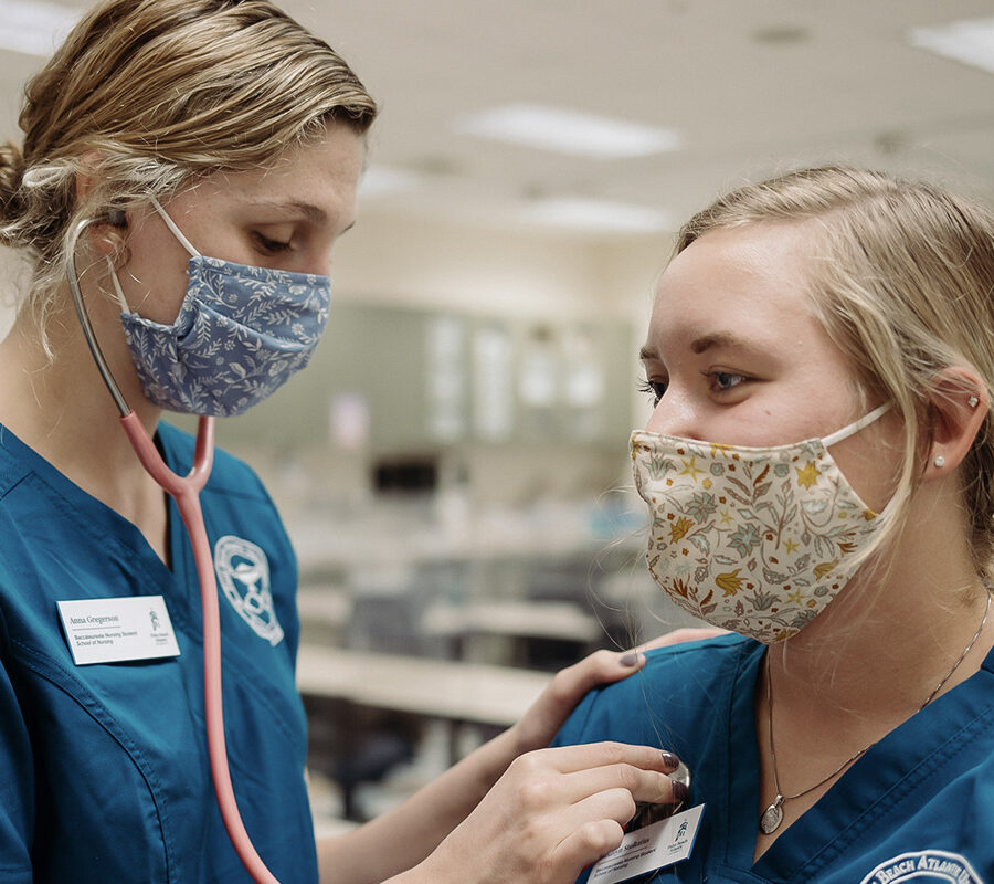 a nursing student listening to the heartbeat of another student through a stethoscope