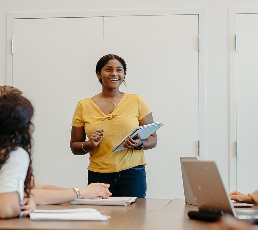 a smiling student presents in class to other students