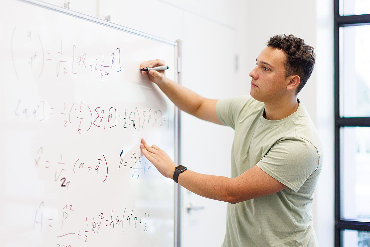 Student from engineering concentration in general engineering program writes equations on a whiteboard.