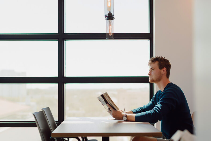 interdisciplinary studies student reads a book at a table near a window.